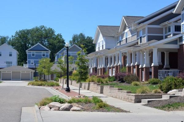 Row of modern townhouses with brick and siding exteriors, landscaped front yards, and a sidewalk under a clear blue sky.