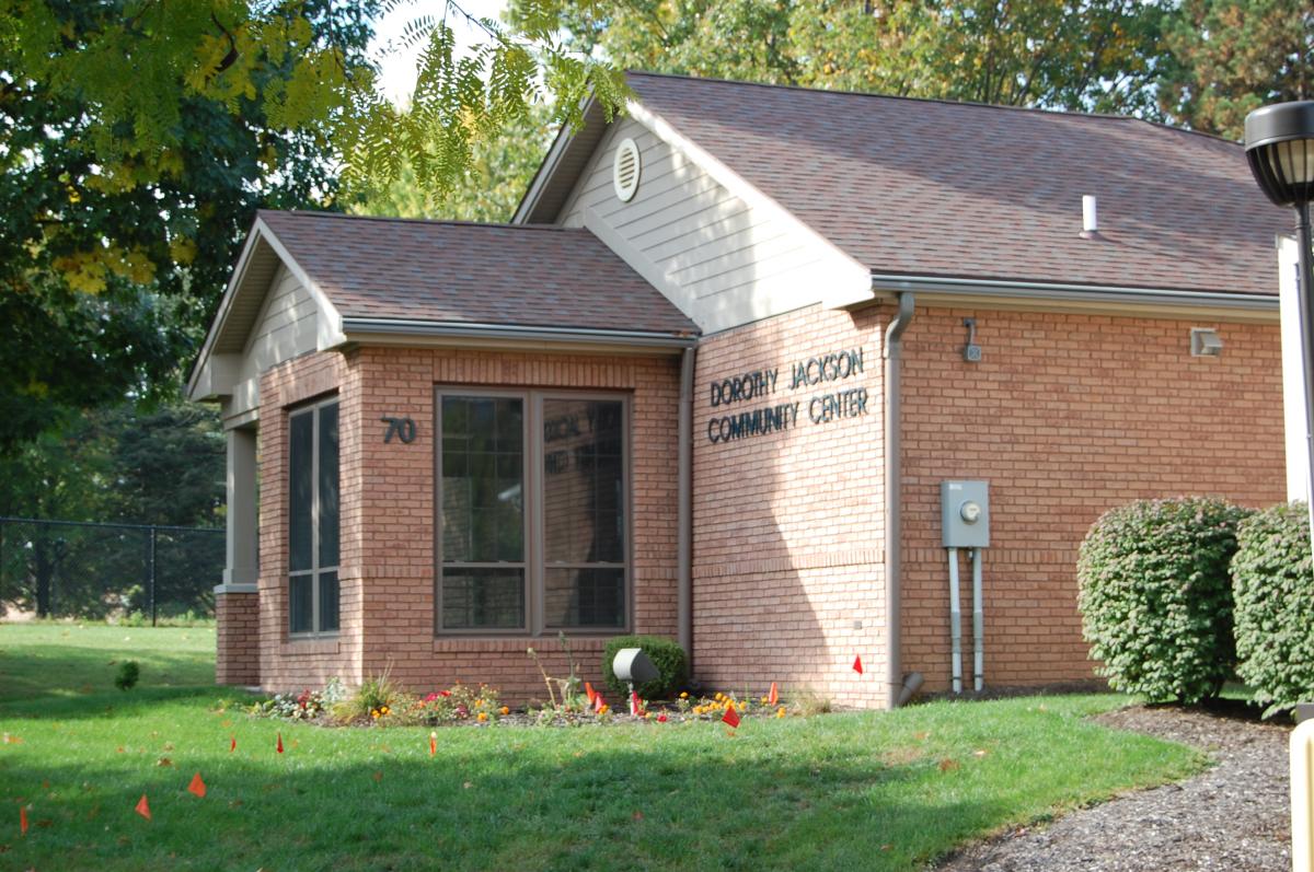 A single-story brick building with a sign reading "Dorothy Jackson Community Center" and address number 70, surrounded by grass and small landscaping flags.