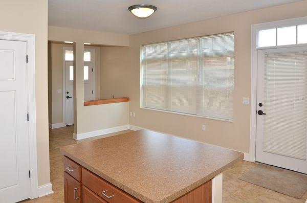 A kitchen with a brown countertop island, tan walls, large window with blinds, and a door with window blinds leading outside.