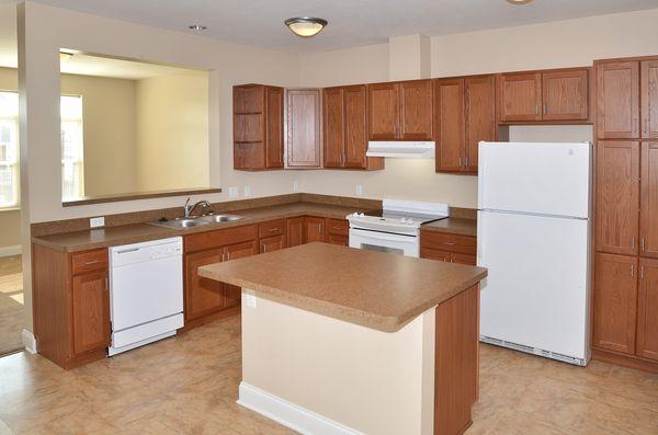 Kitchen with wood cabinets, white appliances including a fridge, dishwasher, and stove, and a central island with a brown countertop under ceiling lights.