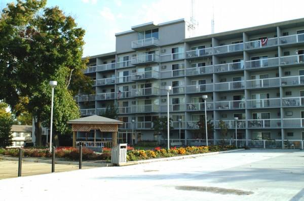 A five-story apartment building with balconies, a wooden gazebo, and garden beds with flowers in front.
