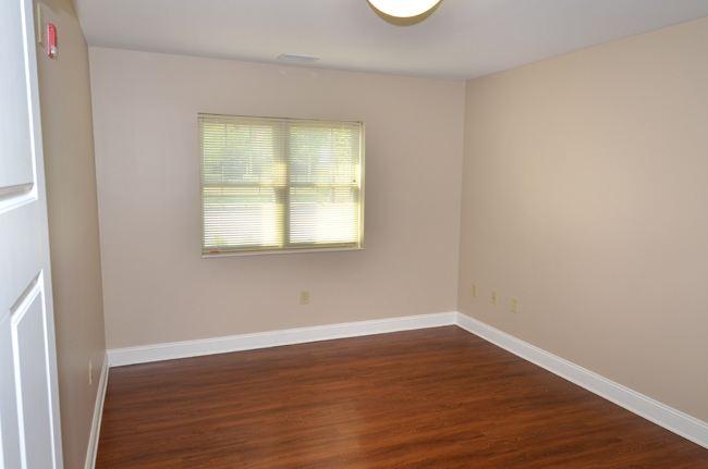 Empty room with beige walls, a window with blinds, wood-style flooring, and a ceiling light fixture.