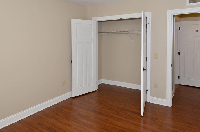 Empty room with wooden floor, beige walls, an open closet with white double doors, and a white door visible to the right.