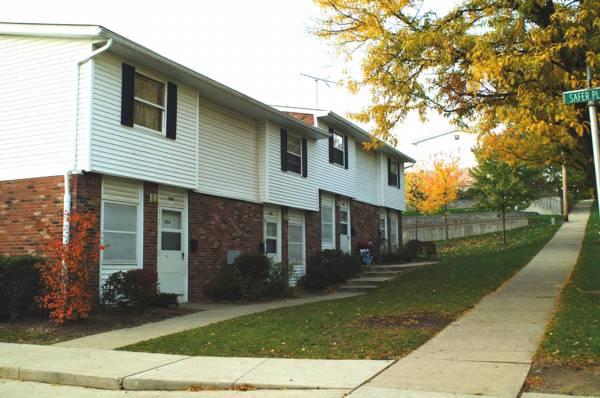 Two-story brick and white siding apartment building with a sidewalk, grass lawn, and tree with autumn leaves.