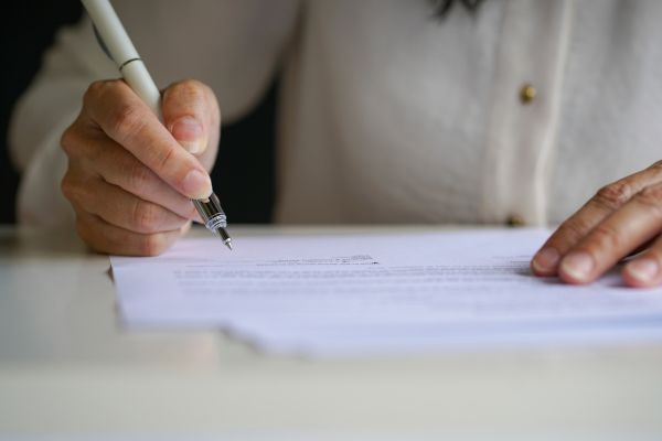 A person holding a pen and signing a document on a desk.