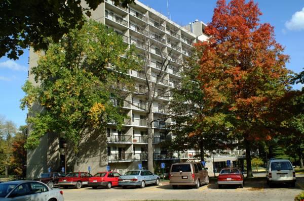 A multi-story apartment building with balconies, surrounded by trees, under a clear blue sky.