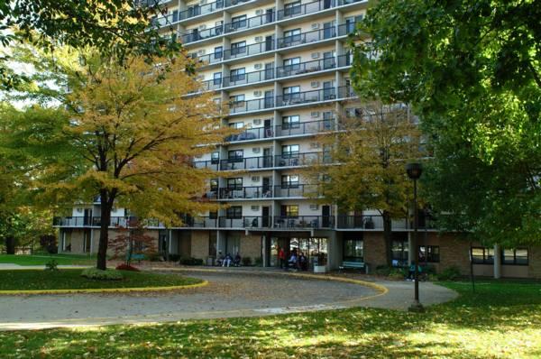 A multi-story apartment building with balconies, surrounded by trees with autumn foliage and a circular driveway in front.