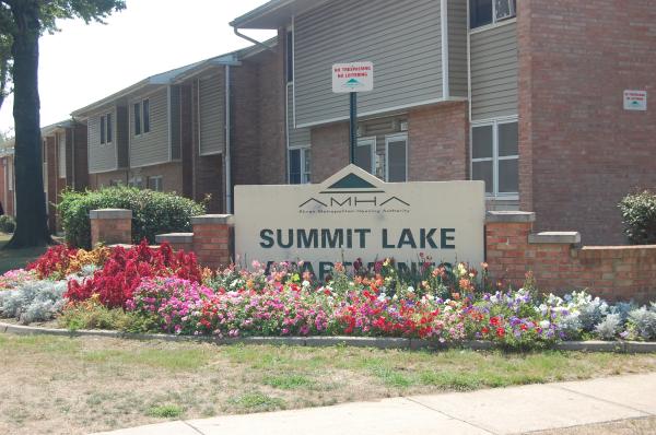 A large sign reads “Summit Lake” in front of an apartment complex with flowers planted along the base of the sign.